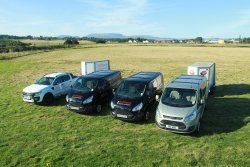 A group of vans are parked in a grassy field.