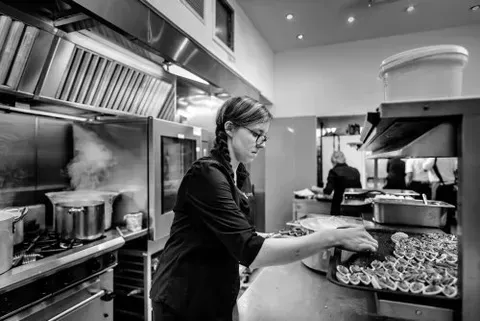 RedPoppy Catering, Inverness, Highlands A woman is cooking food in a kitchen in a black and white photo.
