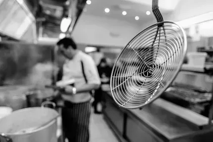 A black and white photo of a chef in a kitchen with a ladle hanging from the ceiling.