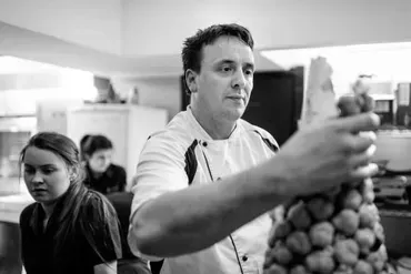 A man in a chef 's uniform is holding a pineapple in a black and white photo.