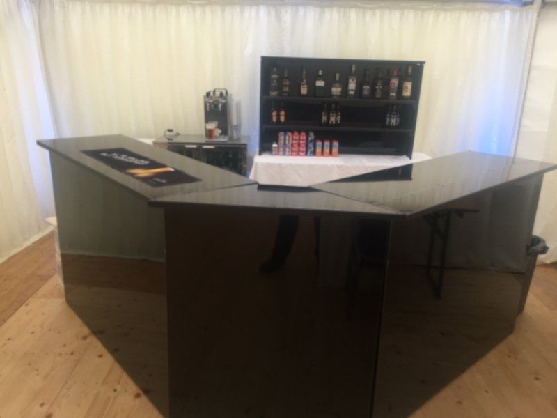 A black bar is sitting in a room next to a shelf with bottles on it.