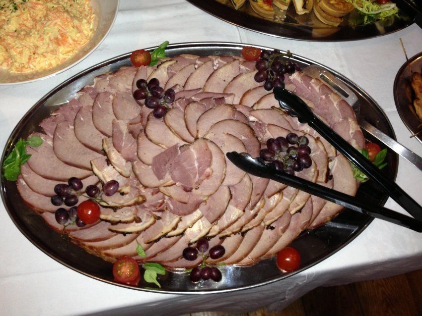 A tray of ham with grapes and tomatoes on a table