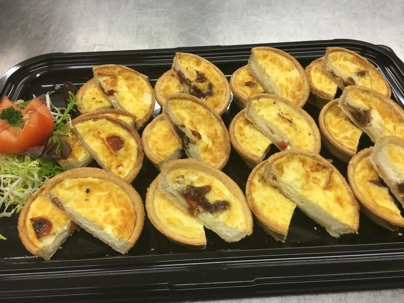A tray of mini quiches with tomatoes and lettuce on a table.