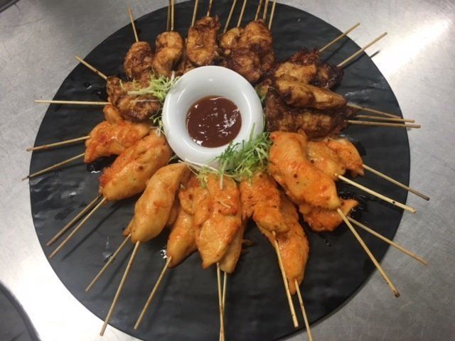 A black plate topped with chicken skewers and sauce