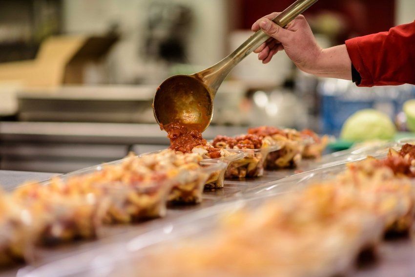 RedPoppy Catering, Inverness, Highlands A person is pouring sauce into a tray of food with a ladle.