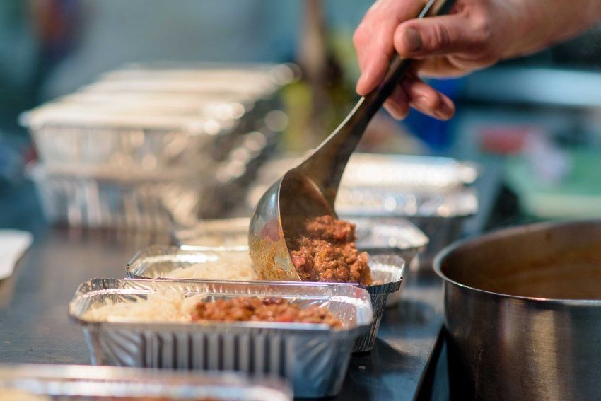 A person is pouring food into aluminum foil containers with a ladle.