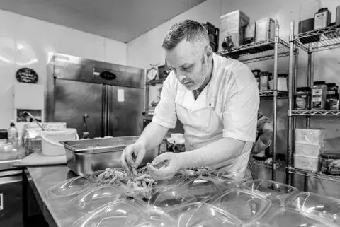 RedPoppy Catering, Inverness, Highlands A man is preparing food in a kitchen in a black and white photo.