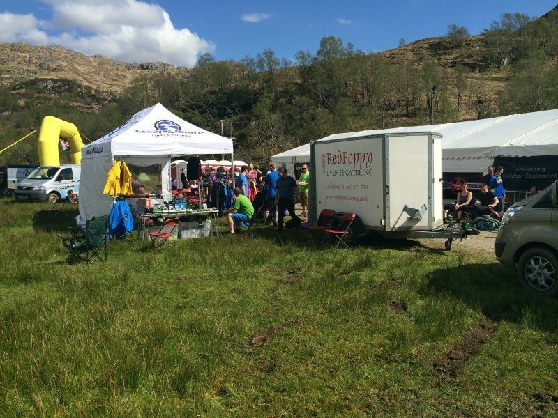 A group of people are gathered in a grassy field in front of a trailer that says ' rickshaw ' on it