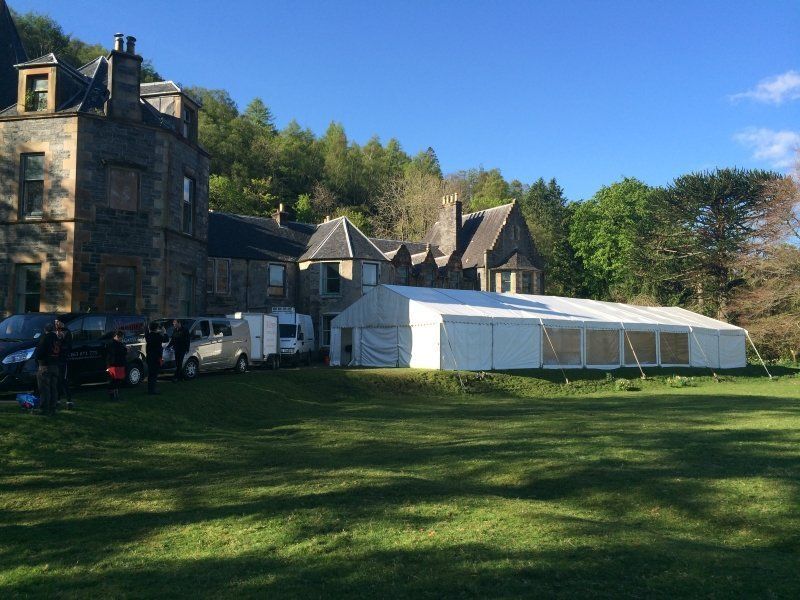 A large white tent is sitting in the grass in front of a large building.