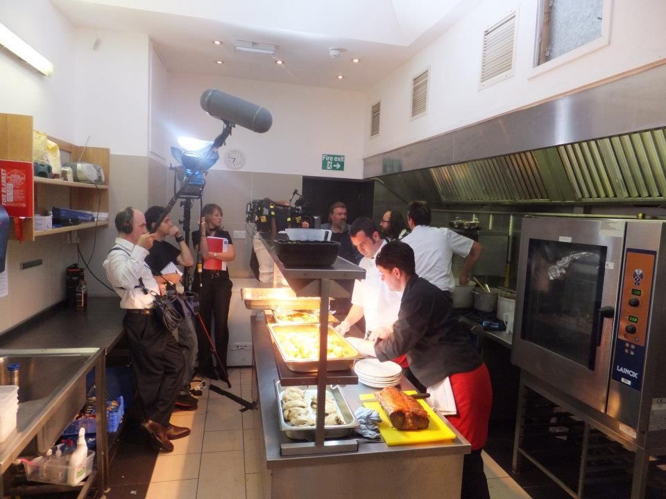 A group of people in a kitchen with a green exit sign on the wall