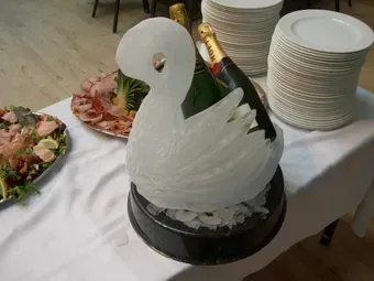 A swan carved out of ice sits on a table next to a bottle of champagne.