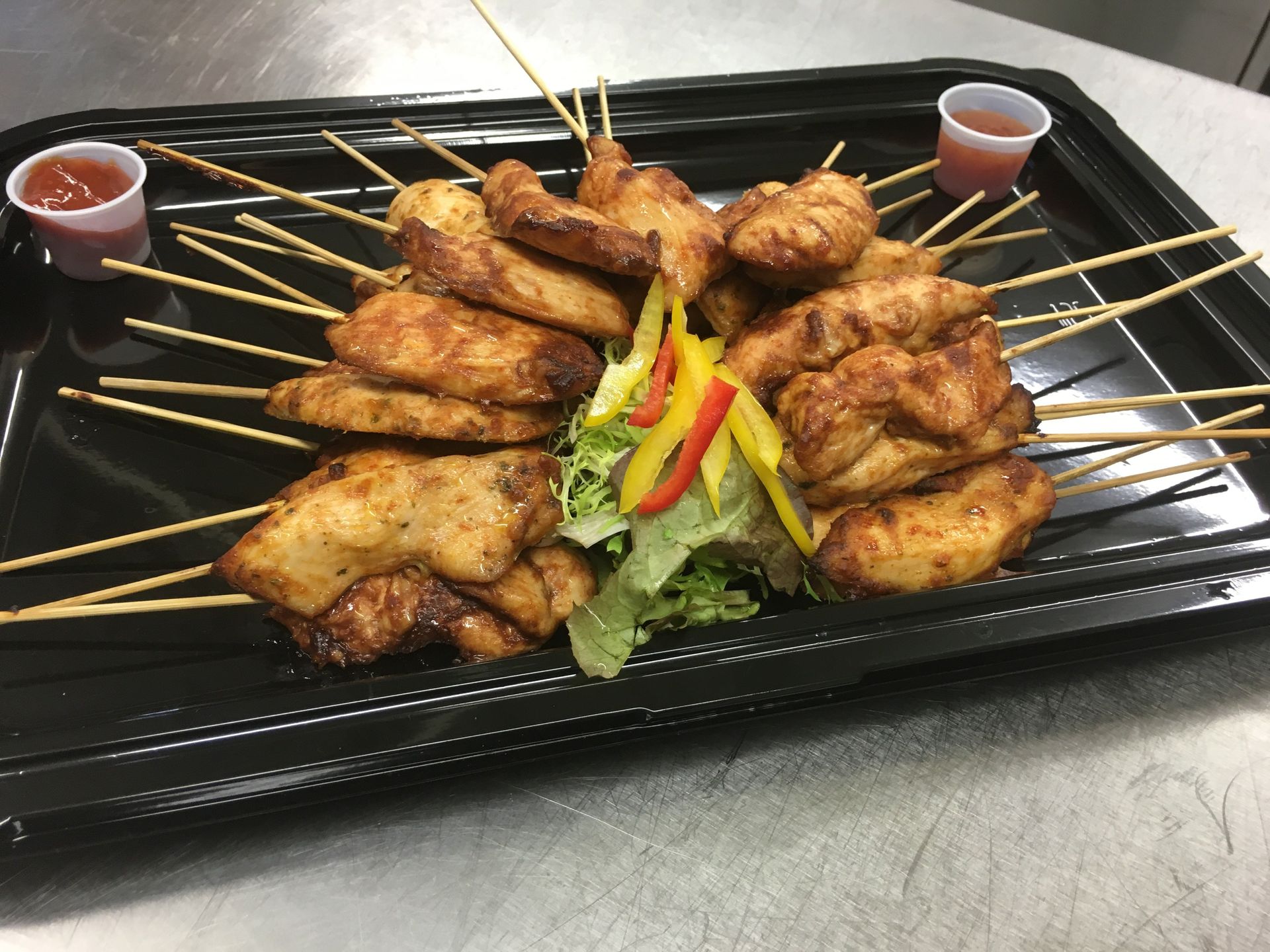 A tray of chicken skewers with sauce on the side