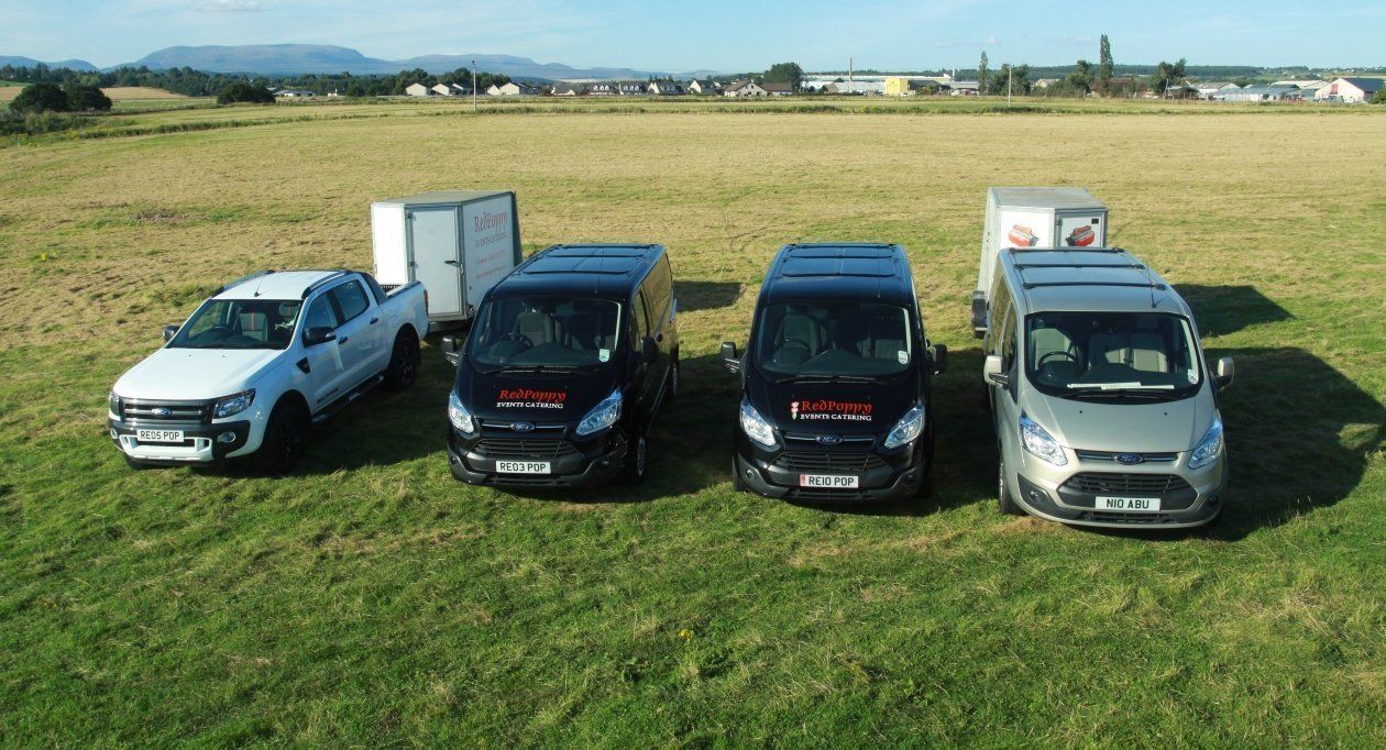 A group of trucks and vans are parked in a grassy field.