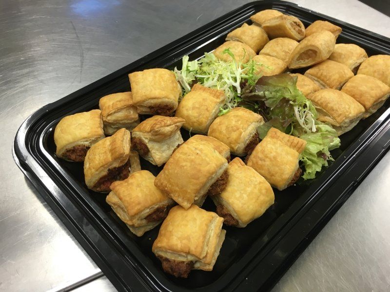 A tray of puff pastry sandwiches with lettuce on a table.