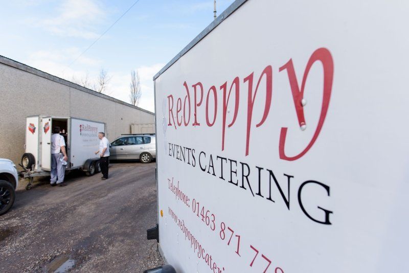 A red poppy event catering trailer is parked in a parking lot