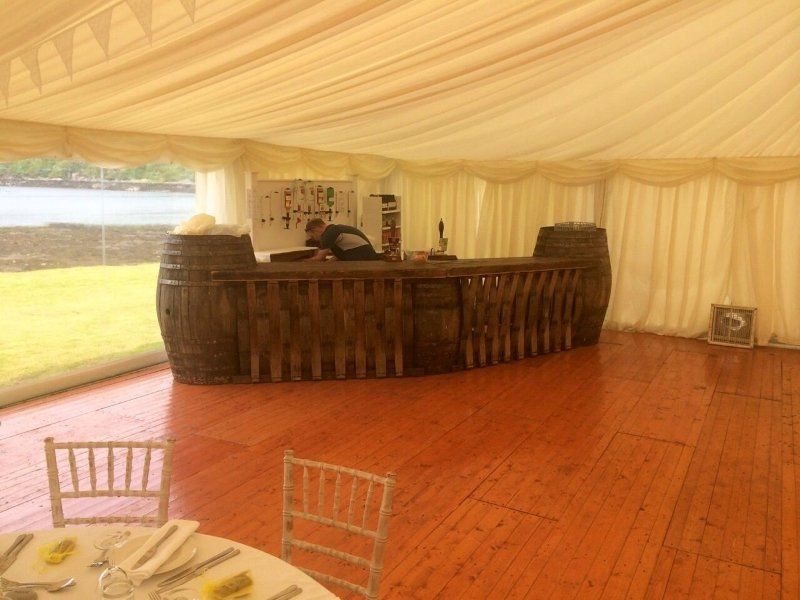 A wooden floor in a tent with barrels and a bar.