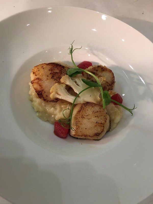 A close up of a plate of food with scallops and cauliflower on a table.