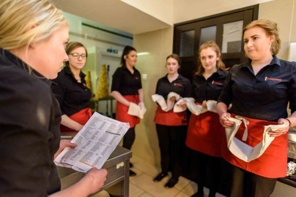 A woman is holding a piece of paper in front of a group of waitresses