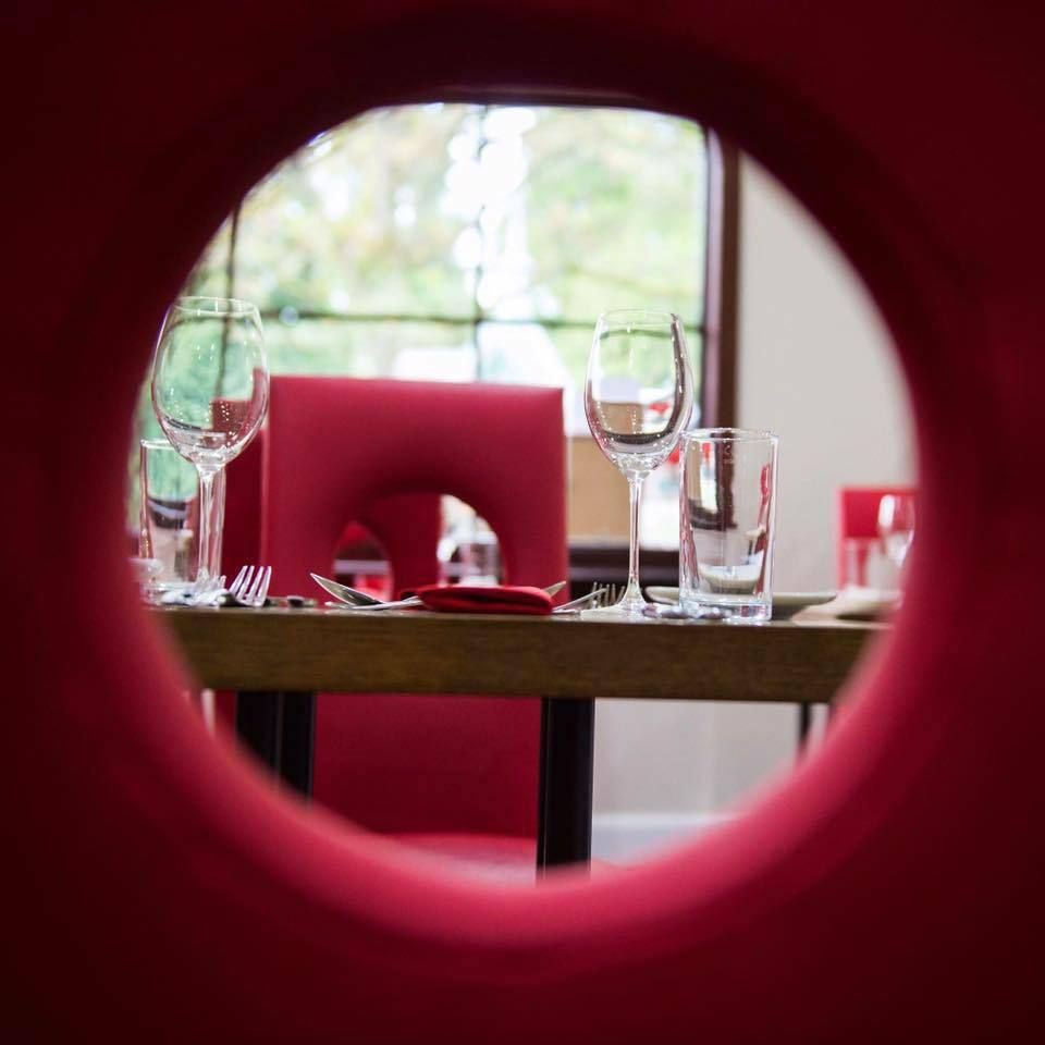 A table with glasses and utensils on it is seen through a hole in a red chair.