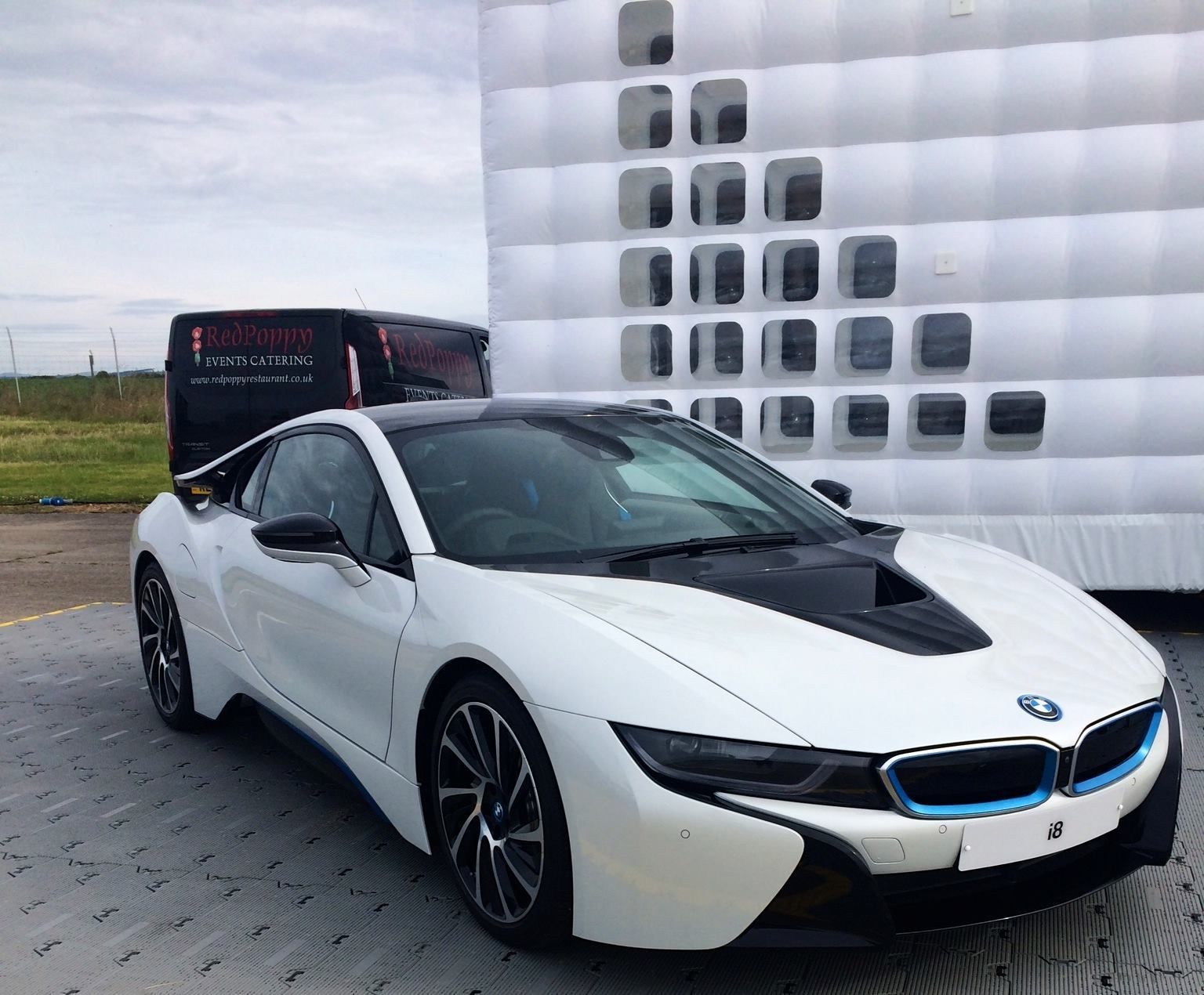 A white bmw i8 is parked in front of an inflatable building