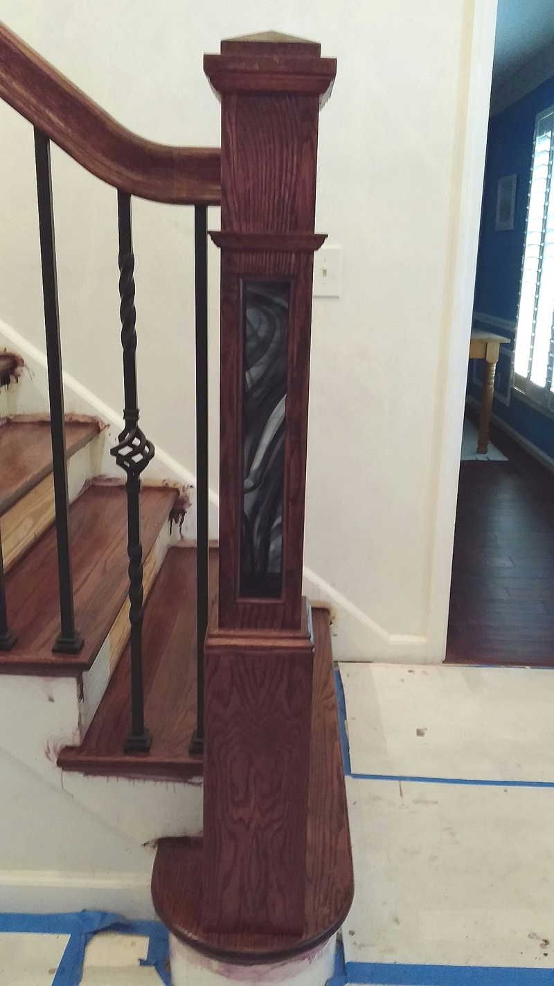 A wooden staircase with a wrought iron railing is being painted.