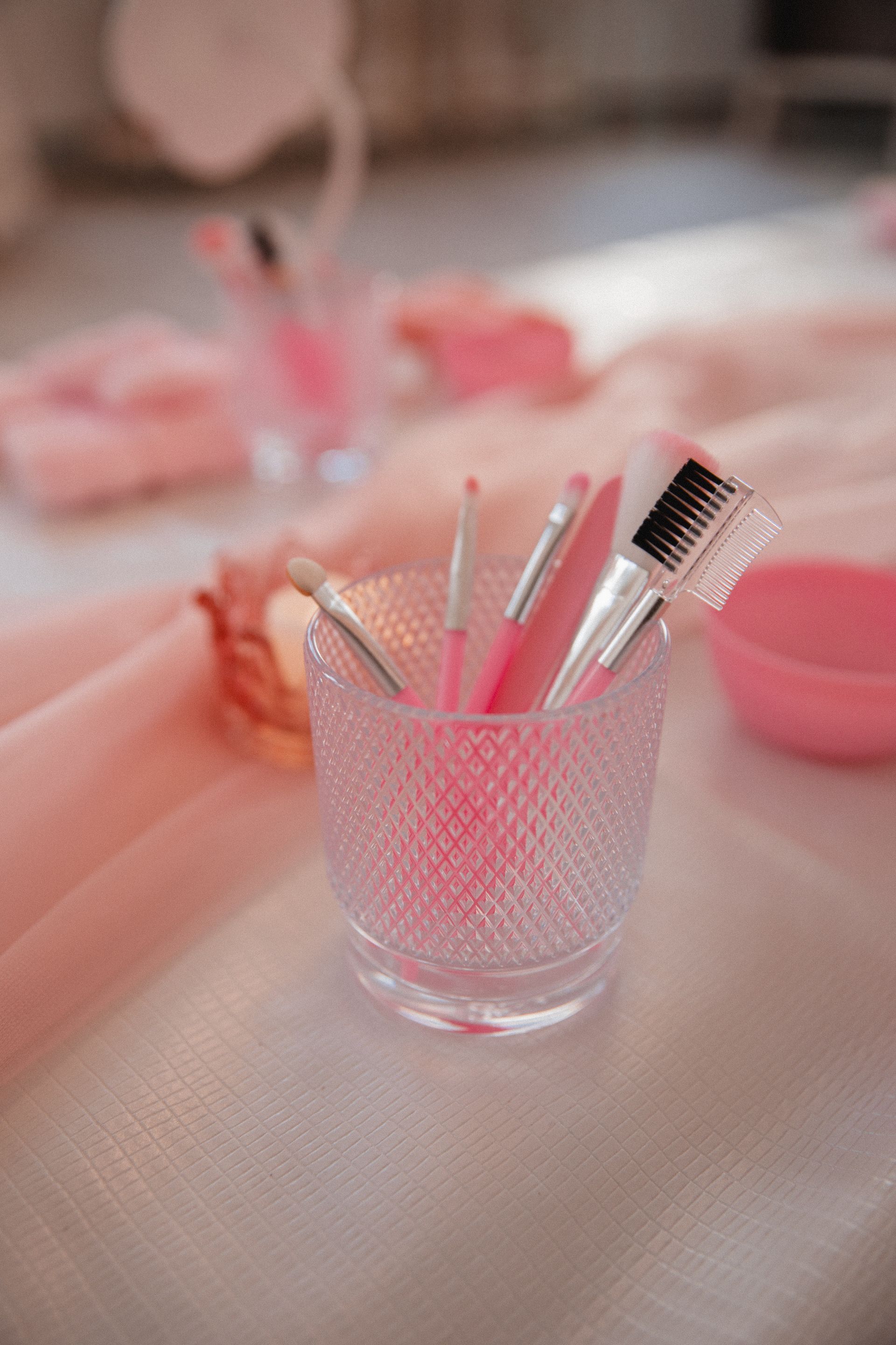 Auf einem Tisch steht ein Glas voller rosa Make-up-Pinsel.