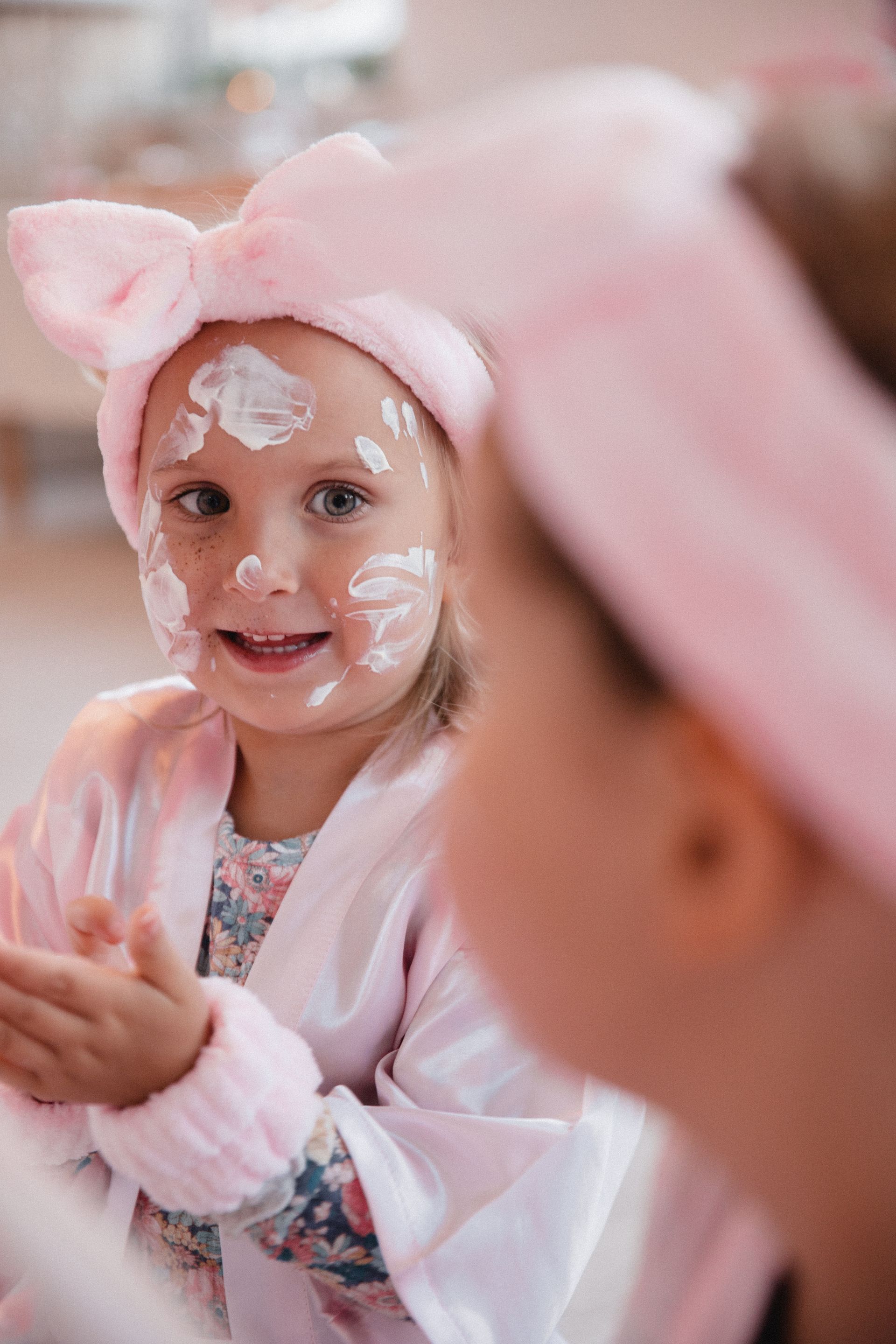 Ein kleines Mädchen mit einem rosa Stirnband und einem rosa Bademantel betrachtet sich im Spiegel.