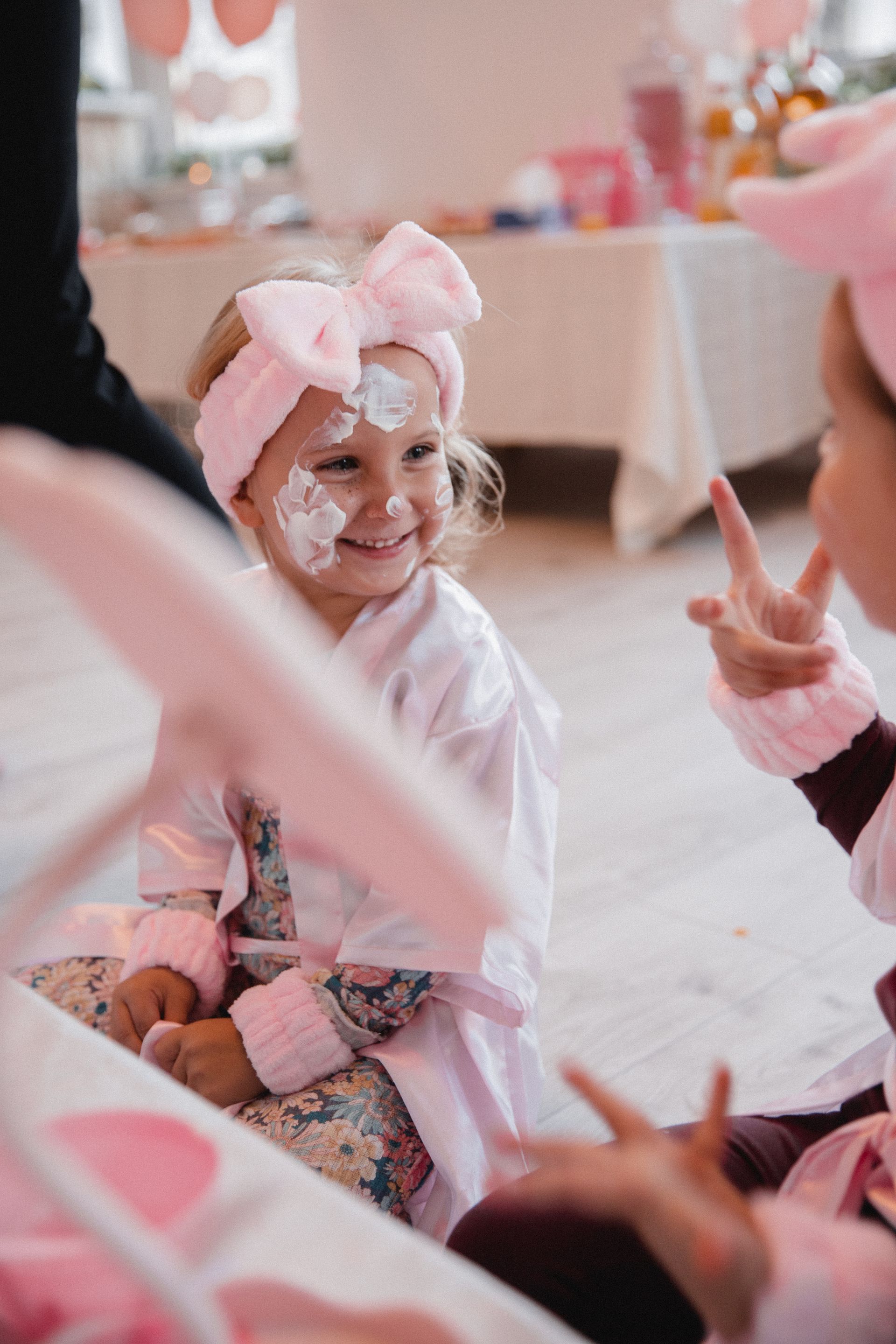 Ein kleines Mädchen in einem rosa Bademantel und mit Stirnband sitzt an einem Tisch.