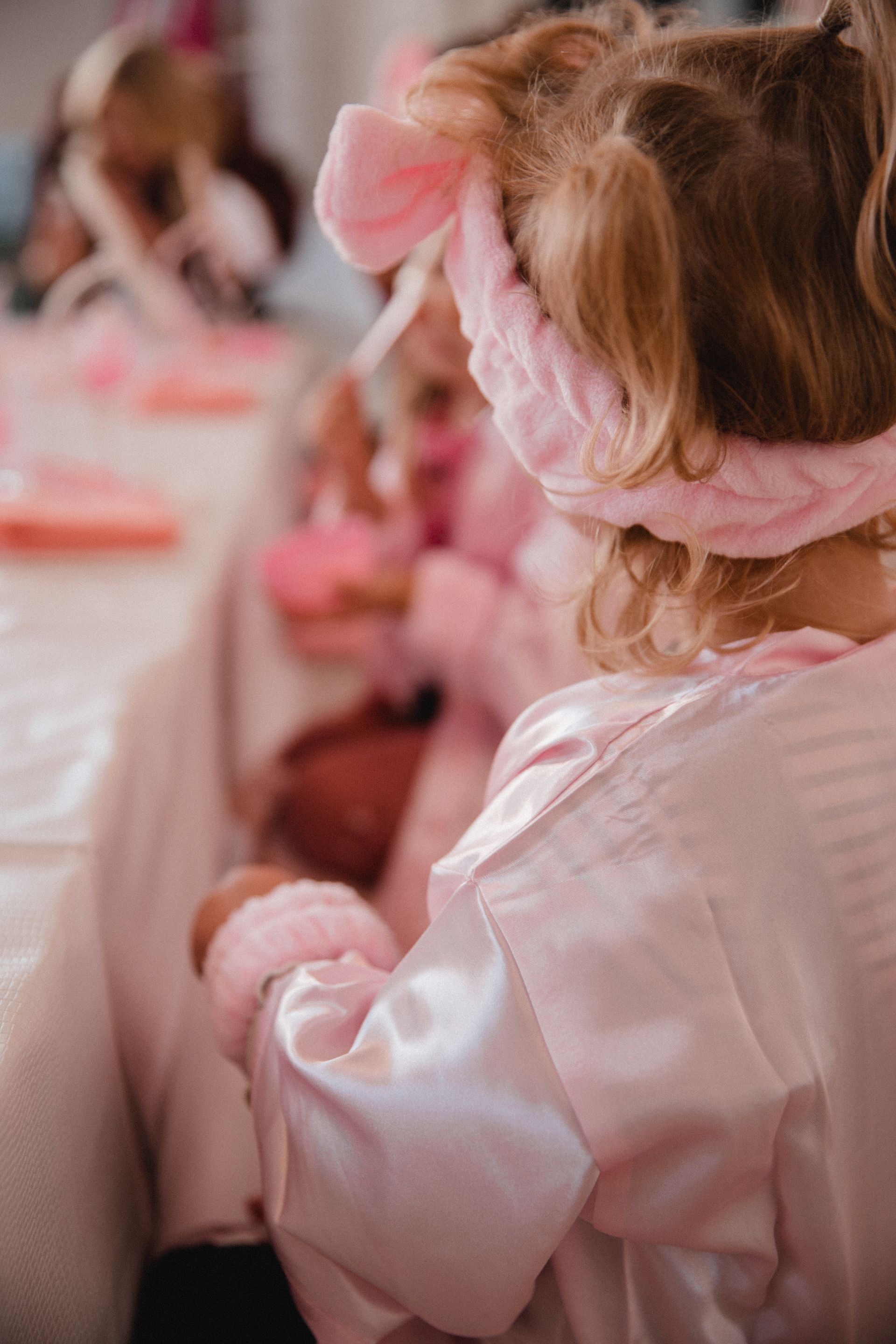 Ein kleines Mädchen mit einem rosa Stirnband sitzt an einem Tisch.