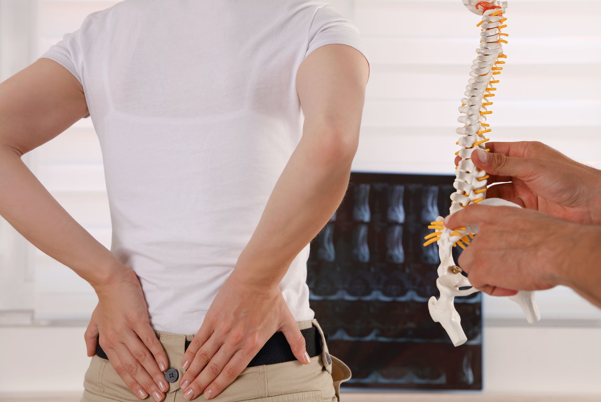 Image of woman holding her lower back and chiropractor holding a model of a spine