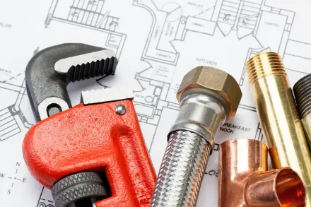 Attrezzi e raccordi idraulici su uno sfondo di progetto: chiave per tubi, pinze e connettori metallici.