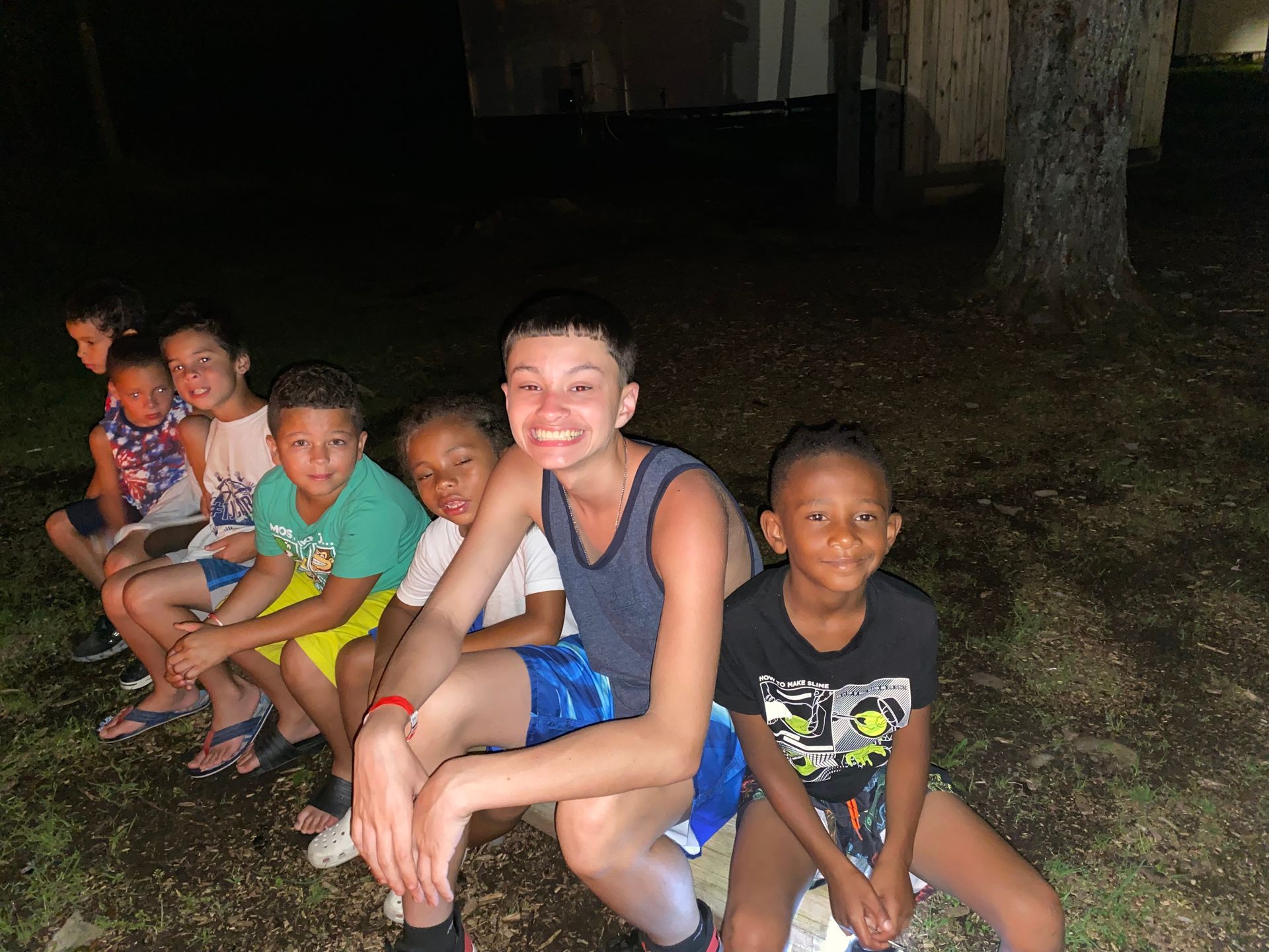 a group of boys sitting on a log beside a campfire