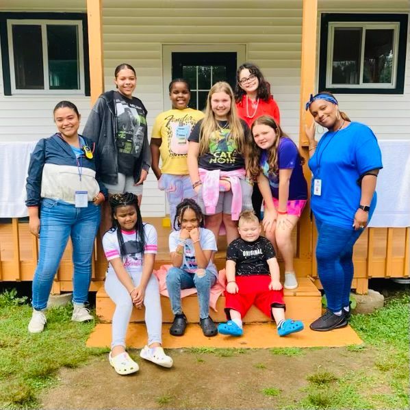 group of campers with their counselors sitting on the steps of their cabin