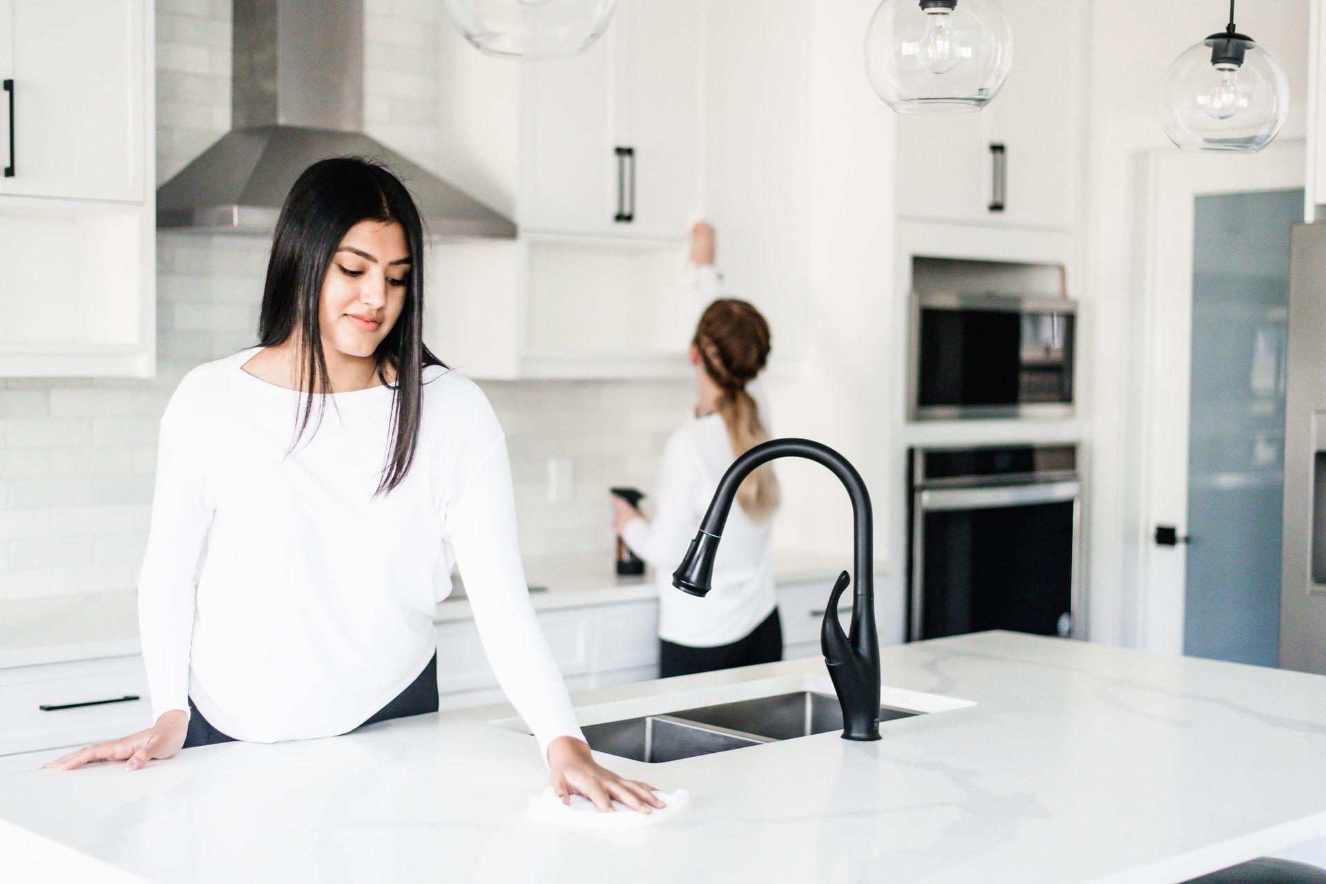 Two women cleaning a bright white kitchen.