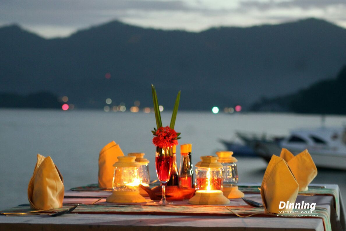 A table with candles and a vase of flowers in front of a body of water