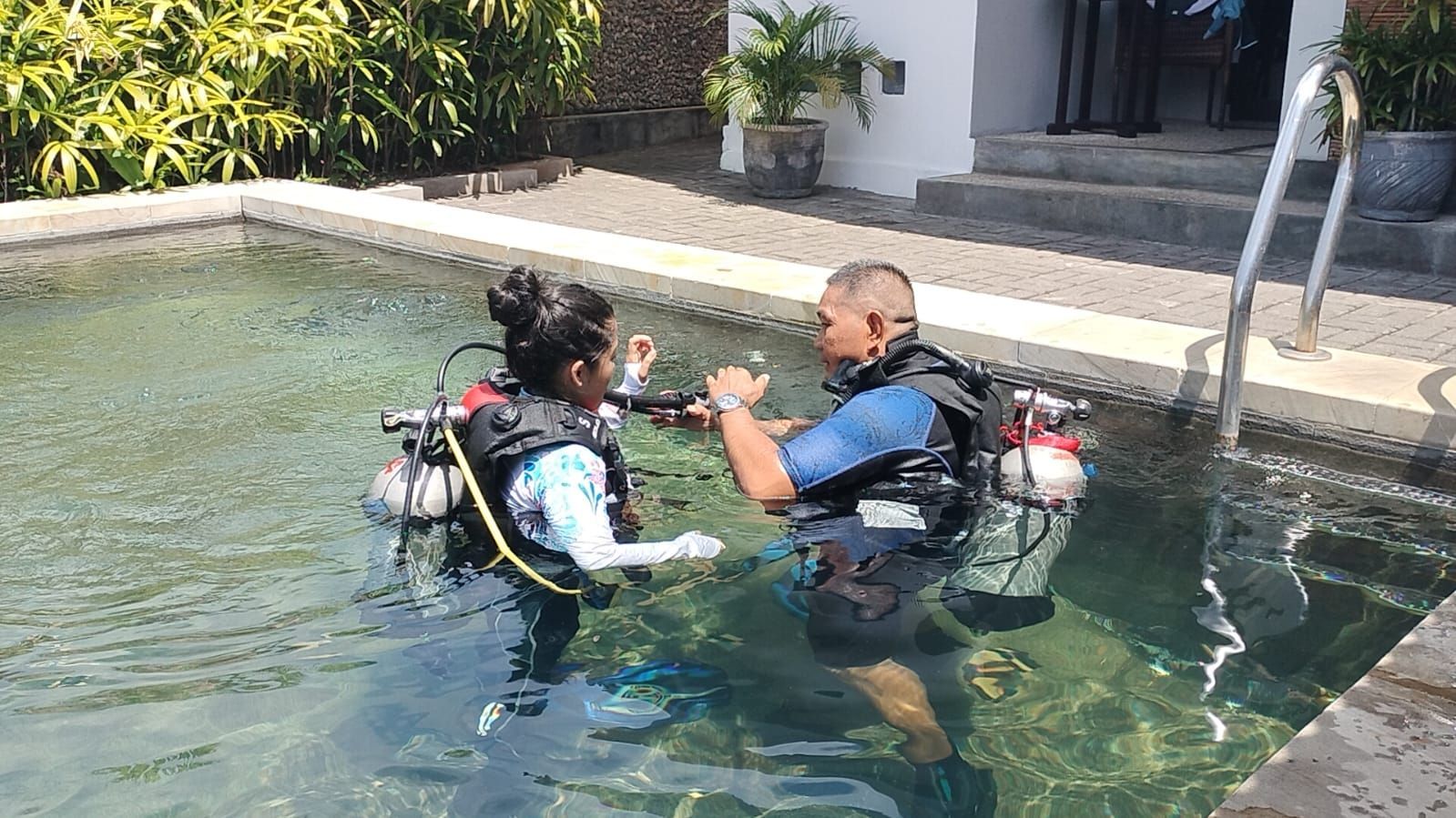 A man is teaching a woman how to scuba dive in a swimming pool.