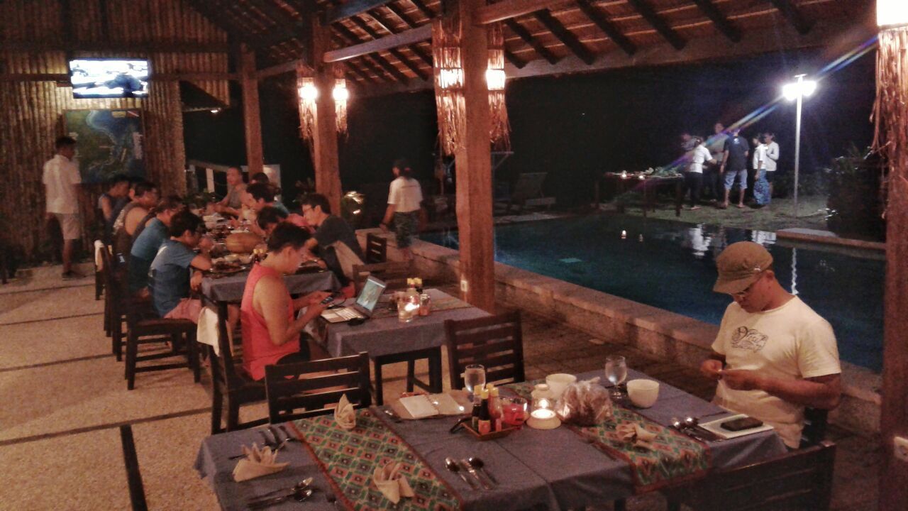 A group of people are sitting at tables in a restaurant with a pool in the background.