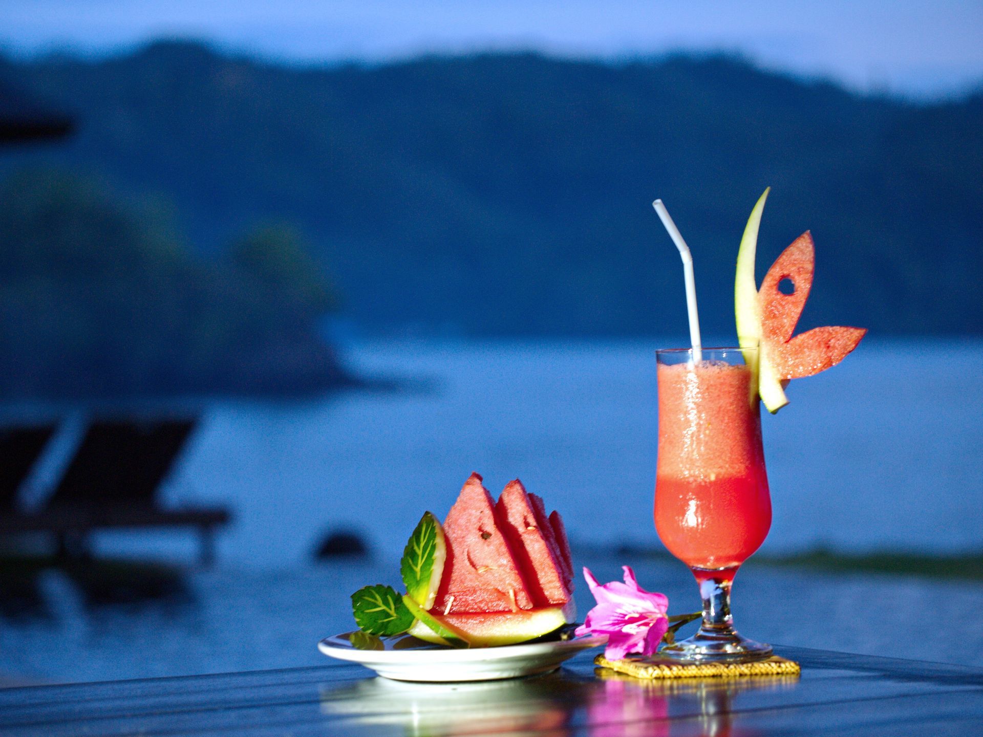 A glass of watermelon juice next to a plate of watermelon slices