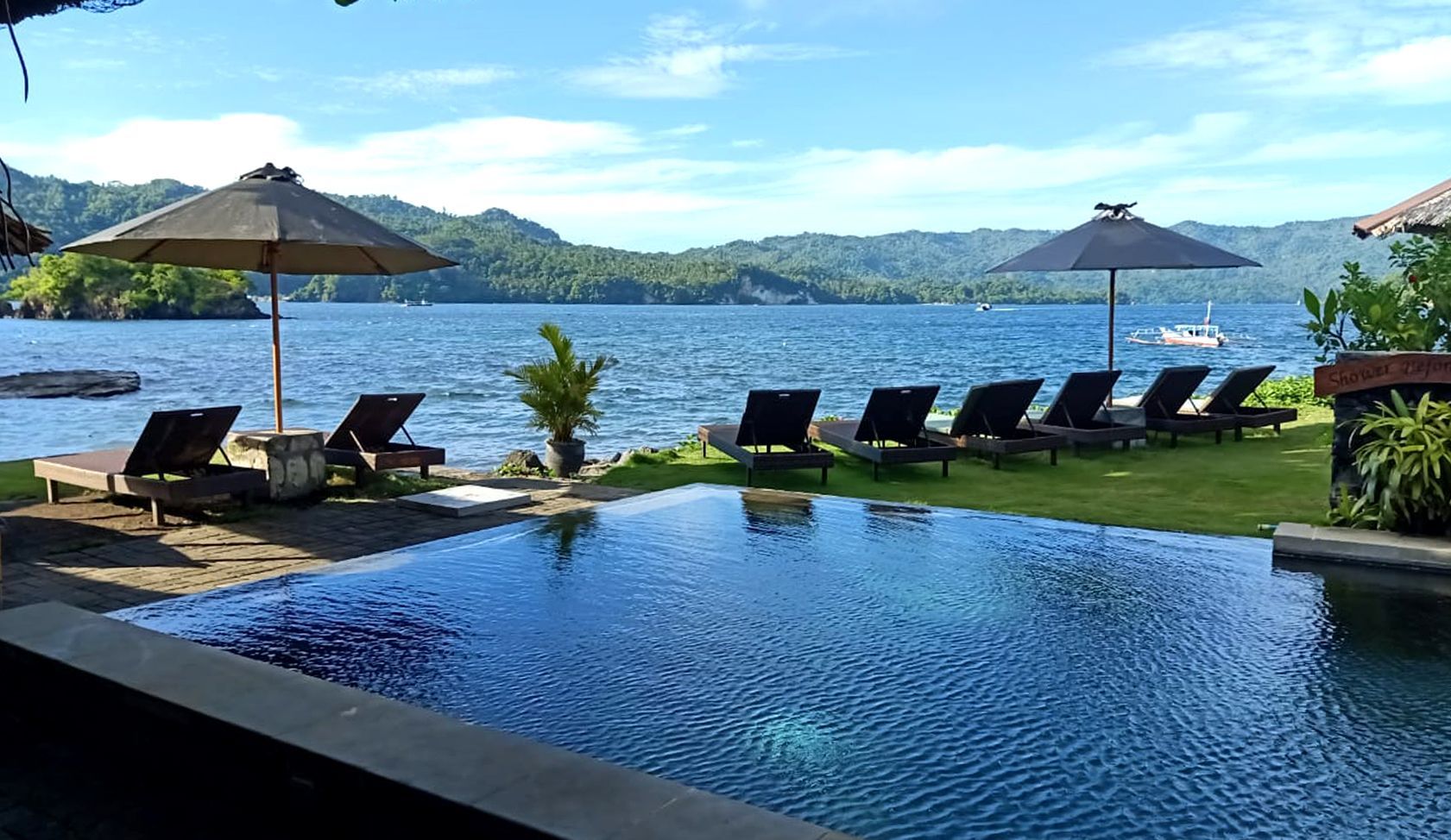 A swimming pool surrounded by chairs and umbrellas next to a body of water.