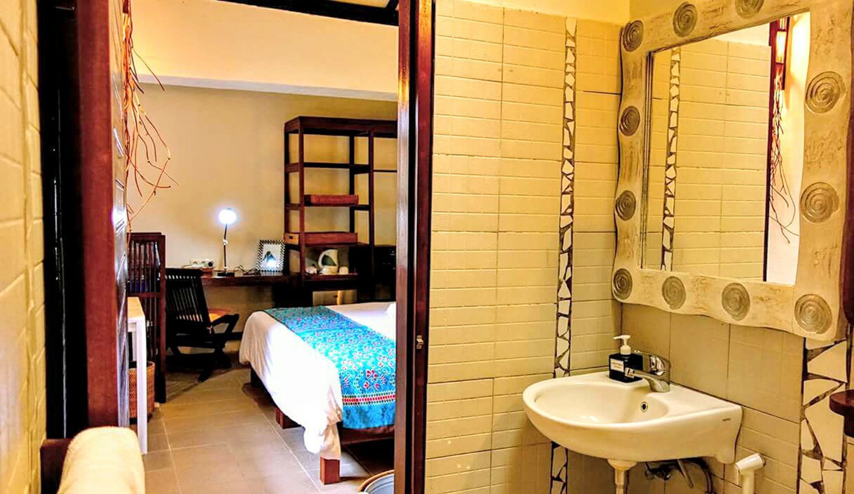 A bathroom with a sink and mirror next to a bedroom.