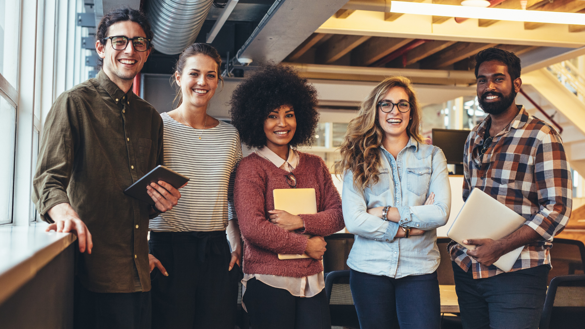 Group of five diverse people smiling in an office setting.