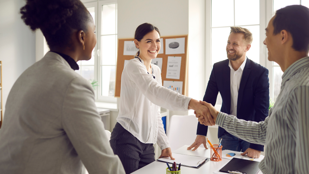 Four businesspeople shaking hands in an office, smiling.