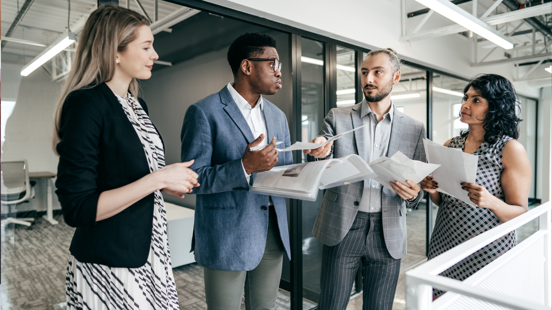 A group of people are standing in an office talking to each other.