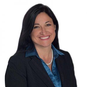 A woman in a suit and pearl necklace is smiling for the camera.