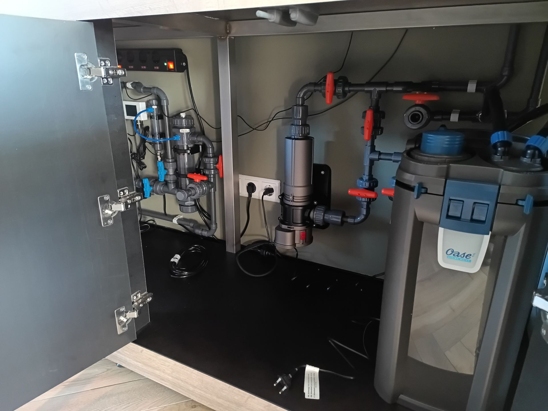 In een kast bevindt zich het filtersysteem van het aquarium, met buizen, kleppen en een potfilter.