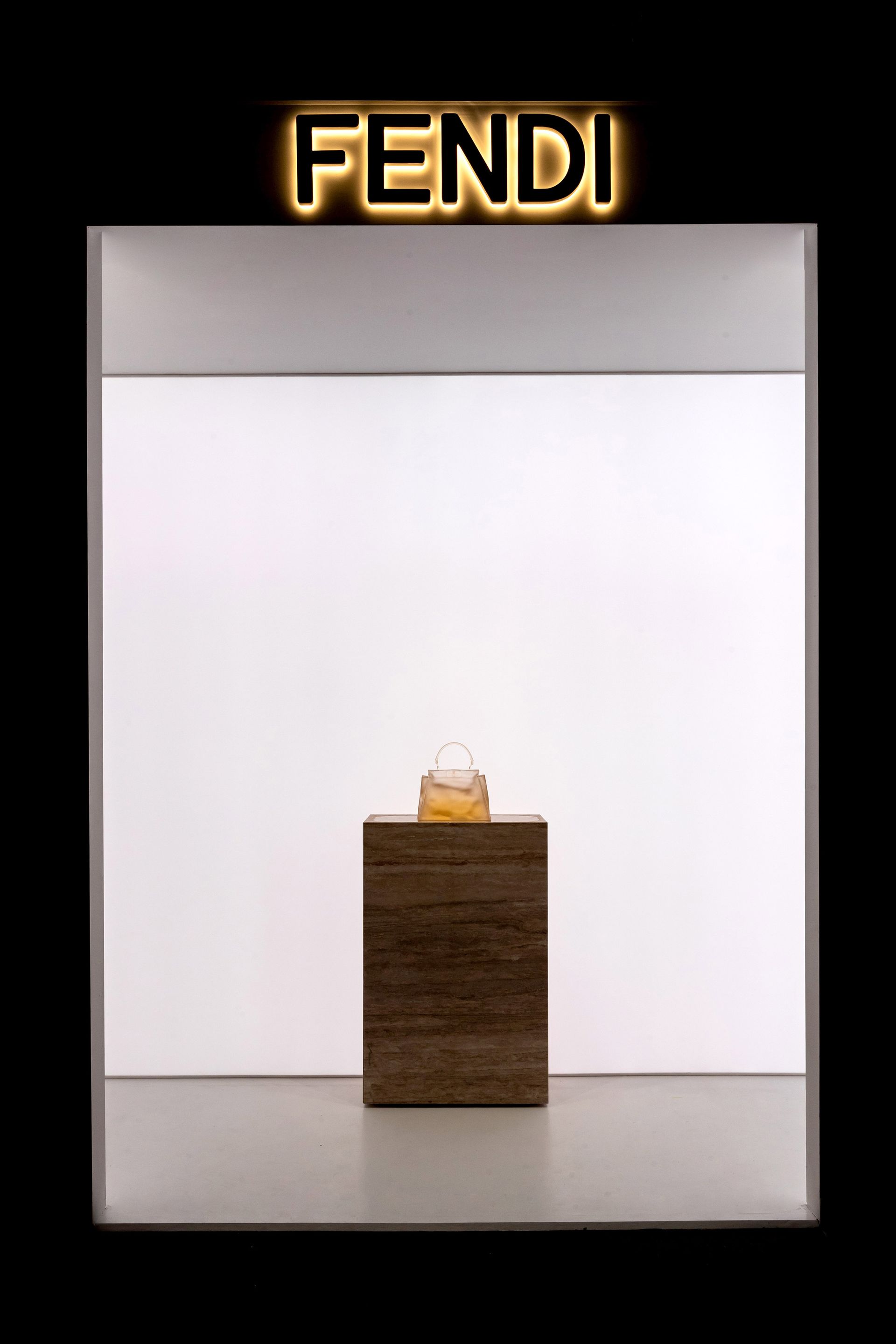 Fendi-display met een fles op een houten blok, verlicht door een oplichtend logo tegen een witte achtergrond.