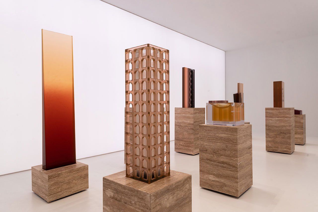 Galerij met sculpturen van verschillende hoogtes, geplaatst op sokkels met structuur in een witte ruimte.