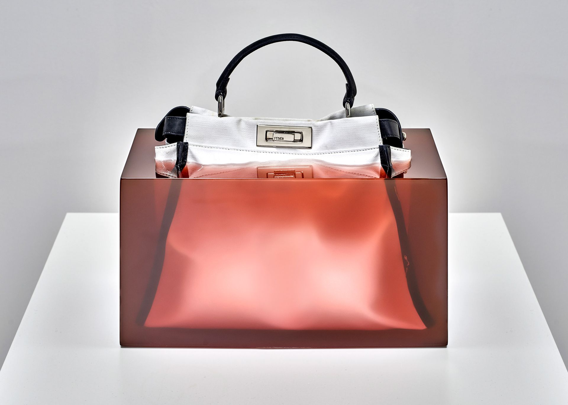 Handtas op een transparante, roodbruine kubus, tegen een witte achtergrond.
