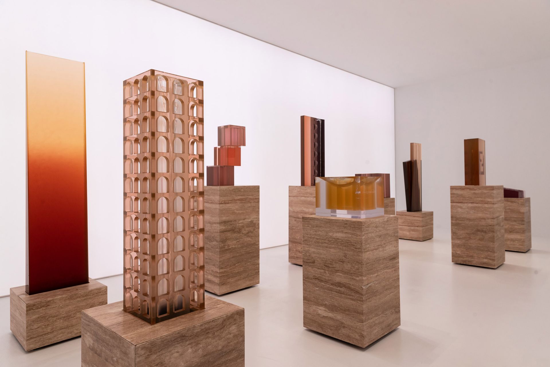 Sculpturen in verschillende vormen en kleuren staan op stenen sokkels in een witte galerij.