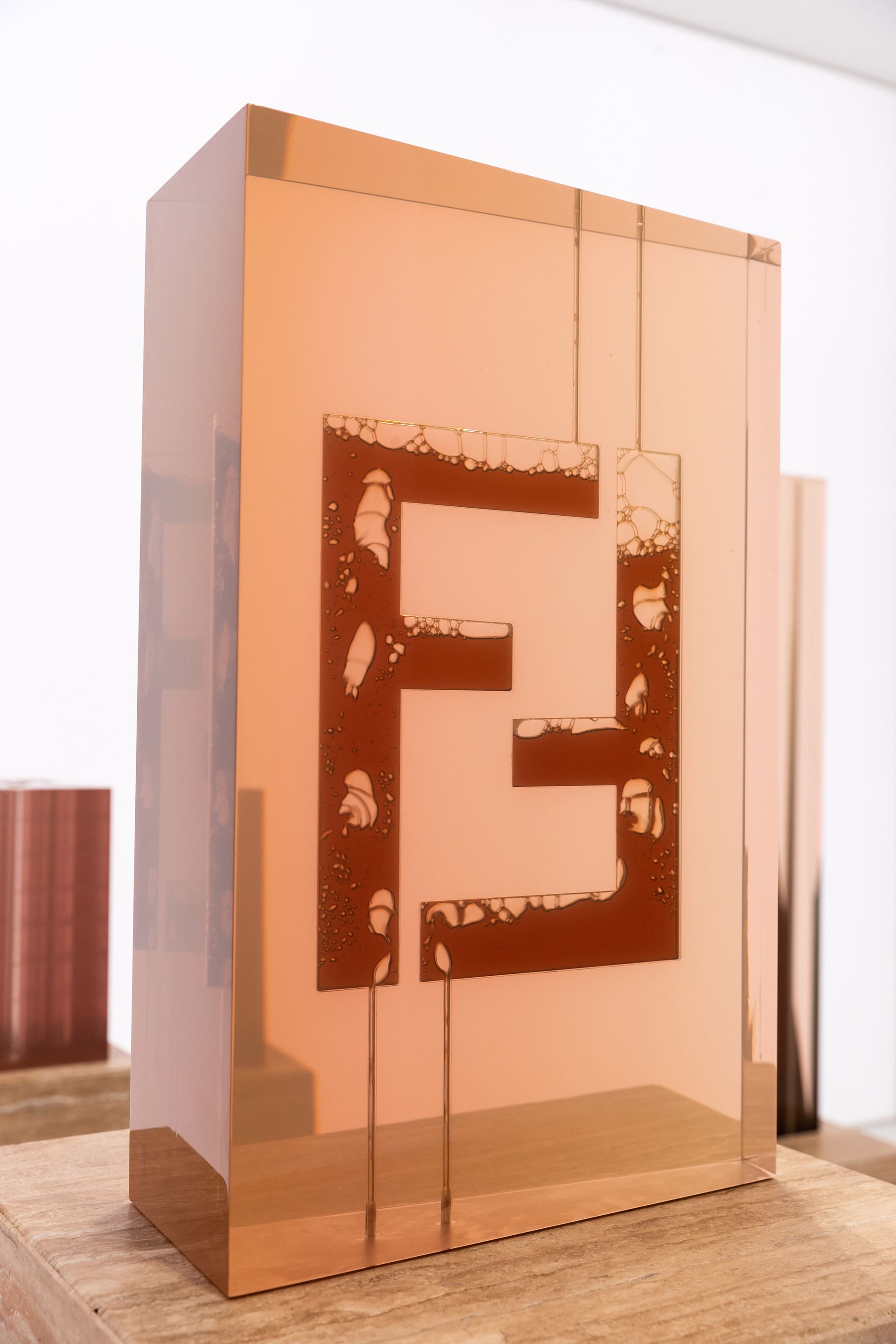 Een bronzen Fendi-logo op een rechthoekige, koperkleurige structuur.